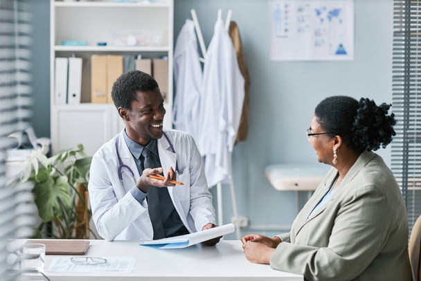 Porträt eines lächelnden schwarzen Arztes im Gespräch mit einer Frau während der Konsultation in der Klinik - Foto, Bild