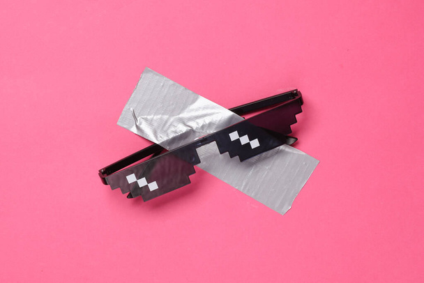 Pixel sunglasses fixed with adhesive tape on a pink background. Conceptual pop, contemporary art, minimalist still life - Photo, Image