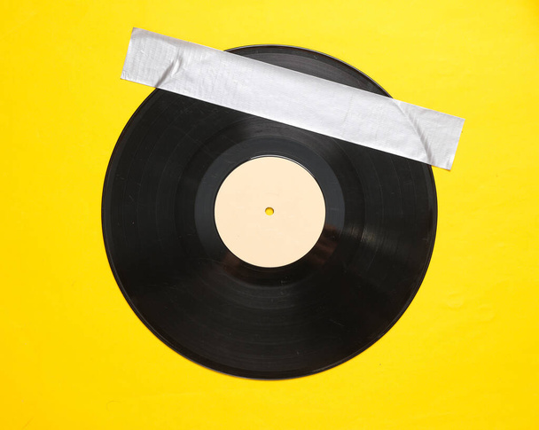 Retro vinyl record fixed with adhesive tape on yellow background. Conceptual pop, contemporary art - Photo, Image