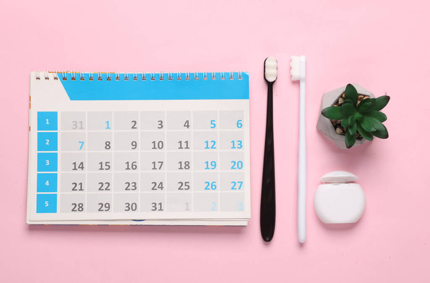 Kalender mit Zahnbürsten und Zahnseide auf rosa Hintergrund. Zahnpflege - Foto, Bild