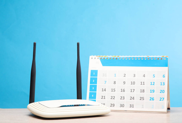 router wi-fi doppia antenna con calendario sul tavolo, sfondo blu - Foto, immagini