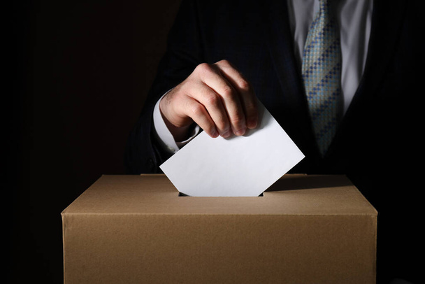 Caja de papel y mano con papel de votación sobre fondo oscuro, primer plano - Foto, Imagen