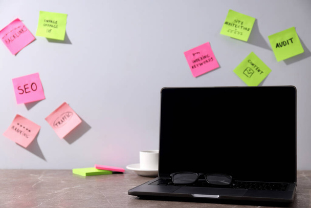 Farbige Papiere mit Wörtern, Laptop, Gläsern und Tasse auf hellem Hintergrund, Platz für Text - Foto, Bild