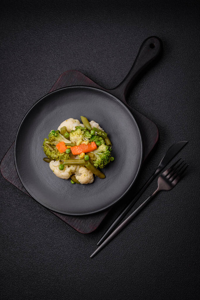 Deliciosas verduras frescas al vapor zanahorias, brócoli, coliflor en un plato negro sobre un fondo de hormigón oscuro - Foto, imagen