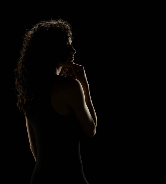 Enigmatische elegantie: gekruld vrouwelijk silhouet op een donkere studio achtergrond - Foto, afbeelding