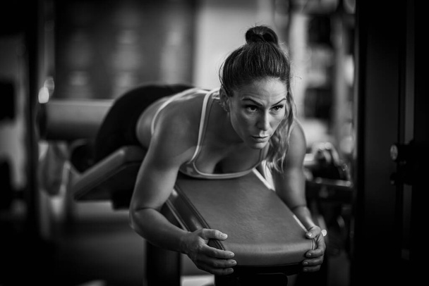 Atleta donna che si allena sulla panchina sdraiata per le gambe in palestra, in bianco e nero - Foto, immagini