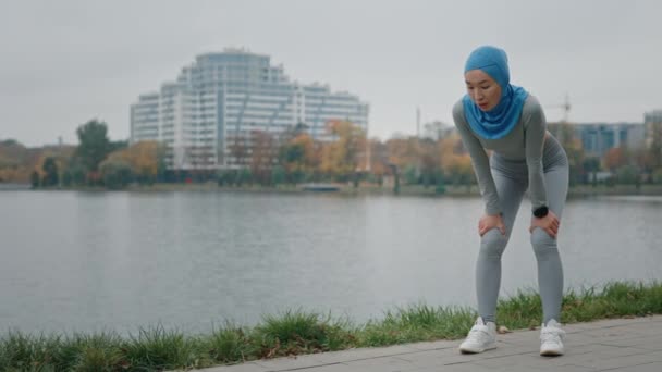 Wyczerpana muzułmańska kobieta sportu stojąca na zewnątrz. Zmęczona pani sportowiec odpoczywa po treningu kardiologicznym. Młoda Sportowiec w odzieży sportowej robi sobie przerwę od ćwiczeń fizycznych. Wytrzymałość na wysiłek fizyczny - Materiał filmowy, wideo