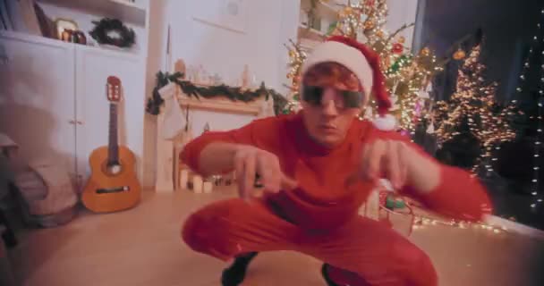 Exhilarated young man in Santa hat and sunglasses performing during party at illuminated home during Christmas - Footage, Video
