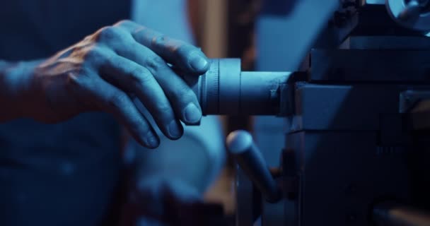 Σε πραγματικό χρόνο μαλακή εστίαση του ανώνυμου αρσενικού πλοιάρχου προετοιμασία τόρνου για την κοπή μετάλλου σε σκοτεινό εργαστήριο με μπλε φωτισμό νέον - Πλάνα, βίντεο