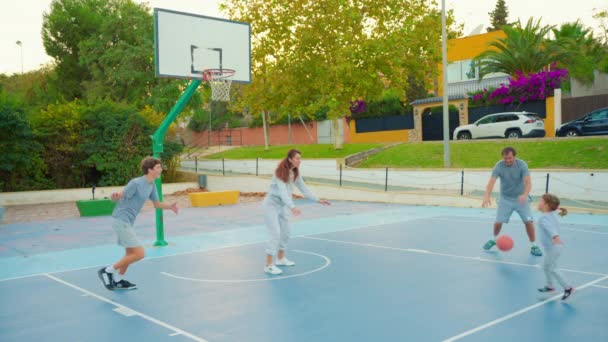 Sport et amitié familiale. Famille multigénérationnelle jouant au basket sur un terrain extérieur. La famille passe son temps libre ensemble à faire du sport et du basket-ball sur le terrain de basket. - Séquence, vidéo