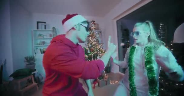 Emocionada pareja joven en gafas de sol bailando en casa decorada durante la Navidad - Metraje, vídeo