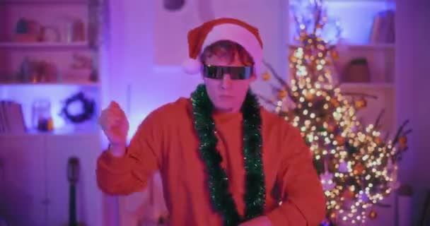 Fiatal férfi télapó kalap és napszemüveg táncol díszített otthon karácsonykor - Felvétel, videó