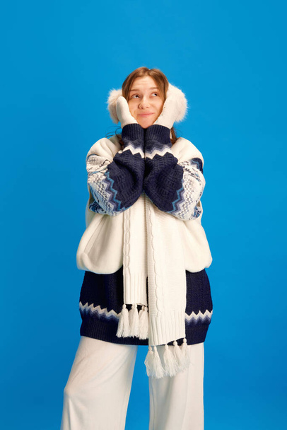 Hermosa joven en un suéter de punto cálido, un traje de calentamiento, sueña con regalos para Año Nuevo sobre fondo azul. Concepto de Navidad, vacaciones de invierno, turismo, vacaciones, moda y estilo. - Foto, Imagen