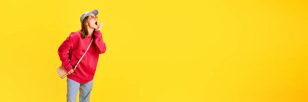 Banner. Atraente menina surpreso, estudante vestido roupas grandes posando contra fundo amarelo com espaço negativo para inserir texto. Conceito de moda e estilo, viajar, cultura, venda - Foto, Imagem