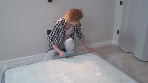 Housewife opens a newly purchased latex mattress from a vacuum roll without air. Mature woman unpacking mattress in new empty apartment without furniture while relocating to new home. Move-in.  - Footage, Video