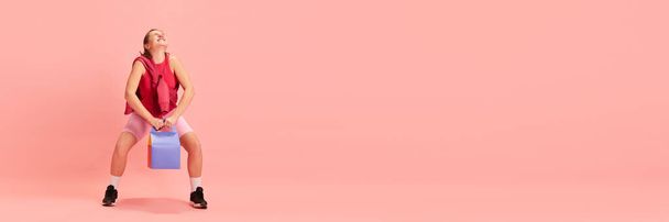Прапор. Молода леді тренується з паперовою кишенею для доставки на пастельний рожевий фон з негативним простором для тексту. Концепція спорту, активний спосіб життя, здорове харчування, фітнес, енергія. - Фото, зображення