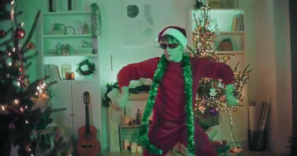 Молодий чоловік з зеленою мішурою навколо шиї танцює в прикрашеному будинку під час Різдва - Кадри, відео