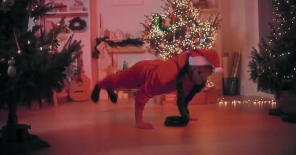 Emocionado joven realizando acrobacias mientras bailaba en el piso en casa decorada durante la Navidad - Metraje, vídeo