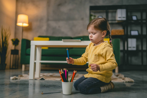Маленькая кавказская девочка играет с карандашами дома - Фото, изображение