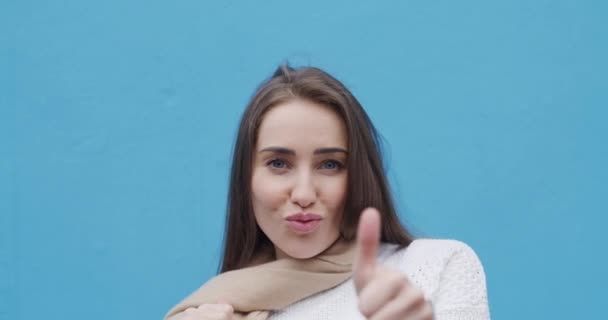 Face, woman and hand gesture in studio for peace, thumbs up or air kiss expression on blue background. Portrait, smile or female model with fun mood, sign language or thank you, pose or confidence. - Footage, Video