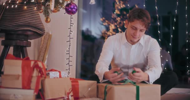 Joven en formales atando cinta en caja de regalo envuelta en casa durante la Navidad - Imágenes, Vídeo