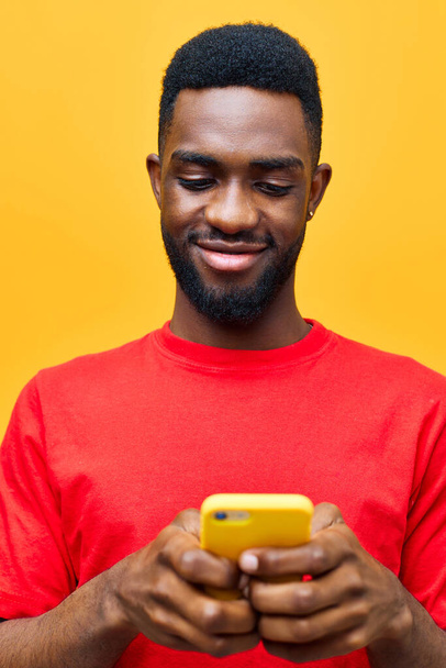muž africký černý tisícileté pozadí červená technologie telefon pestrý muž mladý afro kyberprostor mobilní zpráva prázdný telefon šťastný úsměv mobilní dospělý životní styl žlutá - Fotografie, Obrázek