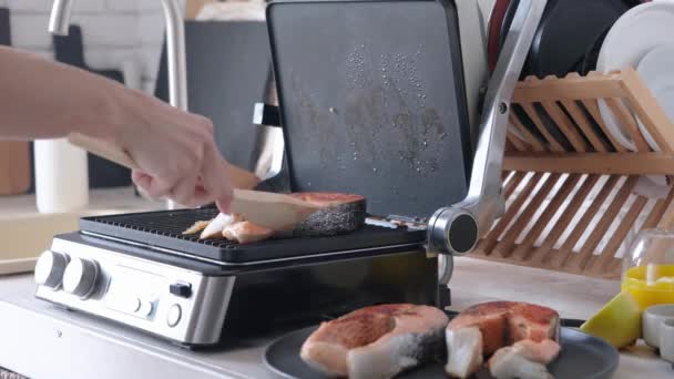 Kobieta gotowanie steków łososiowych na nowoczesnym grillu elektrycznym w kuchni - Materiał filmowy, wideo