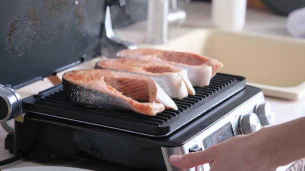 Mujer cocinando filetes de salmón en parrilla eléctrica moderna en la cocina - Imágenes, Vídeo