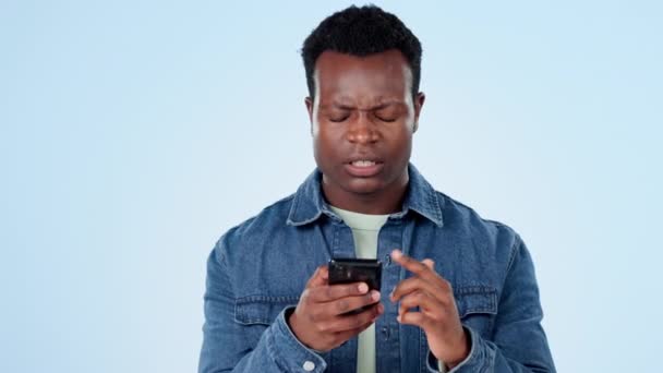 Black man in studio with phone and frustrated reading post, message or notification with connection glitch. Stress, anger and confused person with smartphone, error or spam email on blue background - Footage, Video