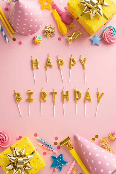 Lovely birthday party composition. Top-view vertical image capturing sweet merengue, wrapped presents, celebratory hats, balloons, confetti, "Happy Birthday" letter candles on pastel pink backdrop - Photo, Image
