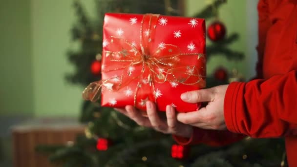 Щаслива приваблива азіатка тримає і показує червоний подарунок камері. усміхнена жінка сидить біля прикрашеної ялинки з різдвяними прикрасами, Різдвом, Новим роком. Високоякісні FullHD кадри - Кадри, відео