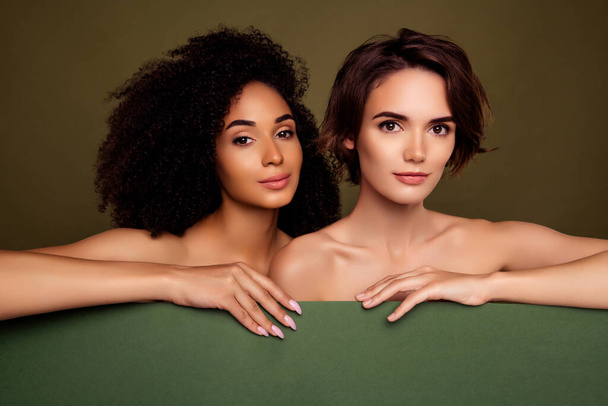 Zdjęcie dwóch perfekcyjnych dziewczyn trzymających deskę, aby promować balsam do pielęgnacji włosów izolowany na tle koloru khaki. - Zdjęcie, obraz