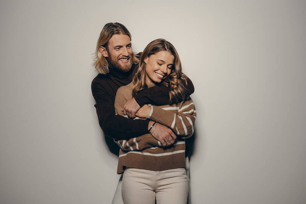 Fashionable young loving couple embracing and smiling on beige background - Fotografie, Obrázek