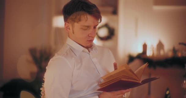 Knappe jongeman die boek leest terwijl hij thuis zit tijdens de kerst - Video