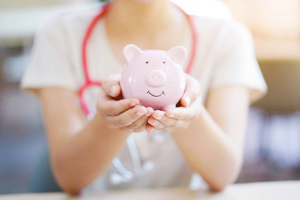 Closeup and crop hands of medical student holding piggy bank on blurred background. - Photo, Image