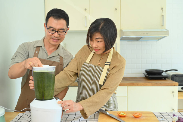 Smiling senior couple making healthy smoothie with blender in kitchen. Healthy lifestyle and dieting concept - Photo, Image