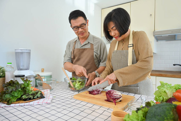 Felice coppia anziana avendo conversazione, rendendo pasto vegan sano insieme in cucina - Foto, immagini