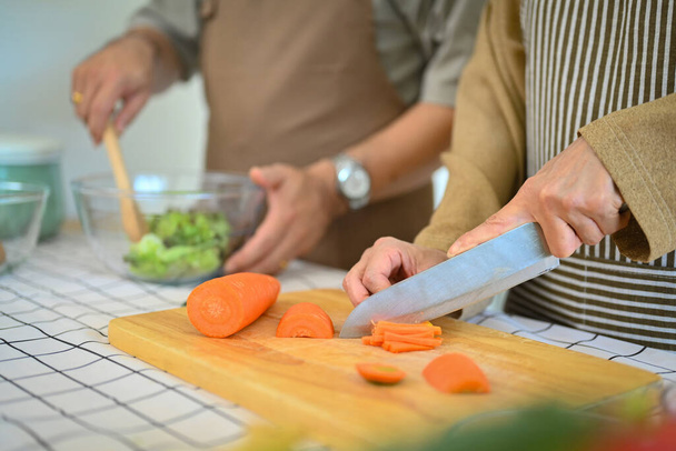 Seniorin hackt Möhren auf Holzbrett für Salat. Konzept der gesunden Ernährung - Foto, Bild
