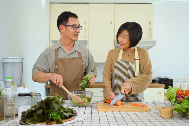 Gelukkig senior paar met gesprek, het maken van gezonde veganistische maaltijd samen in de keuken - Foto, afbeelding