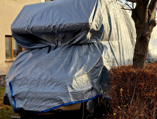the caravan is parked on the street under a lamp and is covered with a tarpaulin over the front of the cabin and windows. kdmping in the city is prohibited and is often fined by the police - Photo, Image