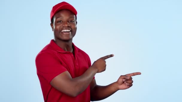 Delivery guy, space or pointing in studio for offer, promotion or ecommerce distribution on blue background. Face of black man talking, show or mockup for post service, shipping or product placement. - Footage, Video
