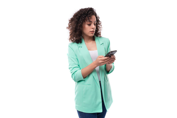 joven elegante delgado modelo femenino caucásico con pelo negro rizado escribe un mensaje en un teléfono inteligente. - Foto, imagen