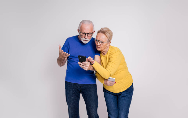 Zazdrosna, ciekawa starsza pani sprawdzająca media społecznościowe męża przez telefon komórkowy na białym tle - Zdjęcie, obraz