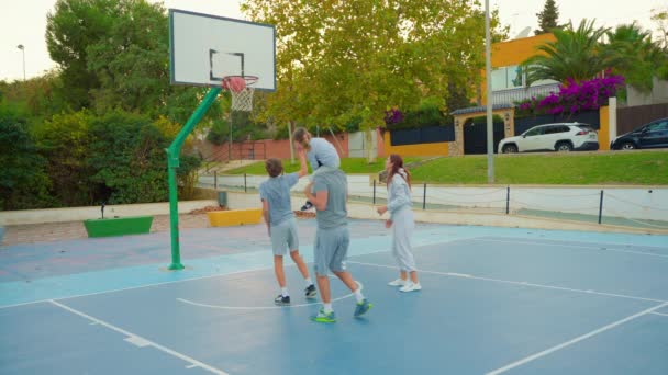 Sport et amitié familiale. Famille multigénérationnelle jouant au basket sur un terrain extérieur. La famille passe son temps libre ensemble à faire du sport et du basket-ball sur le terrain de basket. - Séquence, vidéo