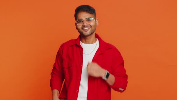 Cheerful lovely happy young Indian man smiling friendly glad expression looking at camera dreaming resting relaxation feel satisfied good news. Arabian bearded guy isolated on orange studio background - Footage, Video