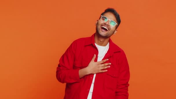 Happy Indian young man laughing out loud after hearing ridiculous anecdote, reaction on funny joke, feeling carefree amused. Positive people lifestyle. Arabian guy isolated on studio orange background - Footage, Video