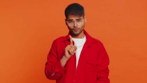 Indischer junger Mann schüttelt den Finger und sagt Nein, sei vorsichtig, schimpfe und gebe Ratschläge, um Gefahren zu vermeiden Fehler, Missbilligungszeichen, widersprechen, Abneigung. Arabischer Kerl isoliert auf orangefarbenem Studiohintergrund - Filmmaterial, Video
