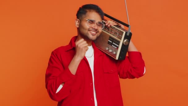 Feliz joven indio que usa el reproductor de cintas retro para escuchar música, pista favorita para bailar disco, divertirse entretenido, fan de las tecnologías vintage. Árabe chico aislado en naranja fondo - Metraje, vídeo