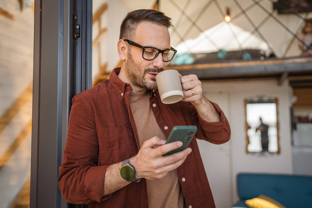 Ein Mann kaukasischen Mann mit Bart und zu Hause verwenden Mobiltelefon für SMS-Nachrichten surfen im Internet oder Video-Anruf-App, während die Arbeit von zu Hause aus Kopierraum reale Menschen - Foto, Bild