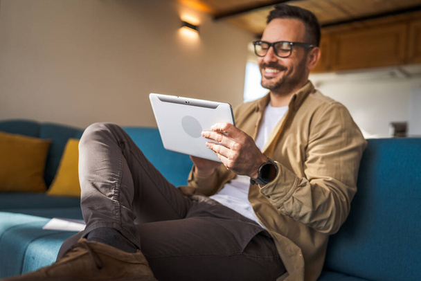 Een man volwassen blanke man houden een digitale tablet werk of surfen op internet vrolijke glimlach thuis zitten vertrouwen dagelijks ochtend routine kopiëren ruimte echte persoon - Foto, afbeelding